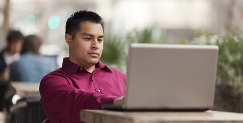 man in red button up shirt applies to MBA program on his laptop