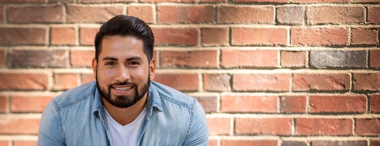 Male Chico State student smiling in front of brick wall on campus
