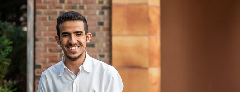 Male Chico State student in white button-down shirt standing in front of brick building on campus