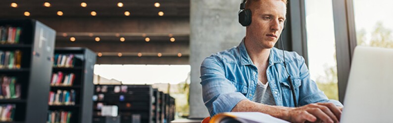 Student wearing headphones and working on a laptop at a library