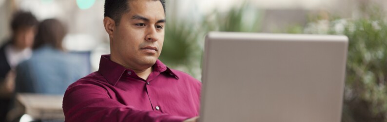 man in red button up shirt applies to MBA program on his laptop
