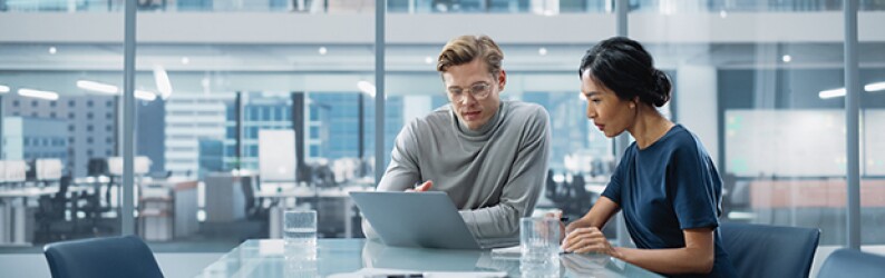 Man and woman sit at table looking at a computer screen.