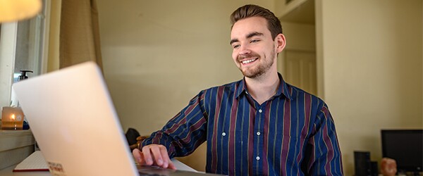 Business student smiling while completing coursework on laptop at home