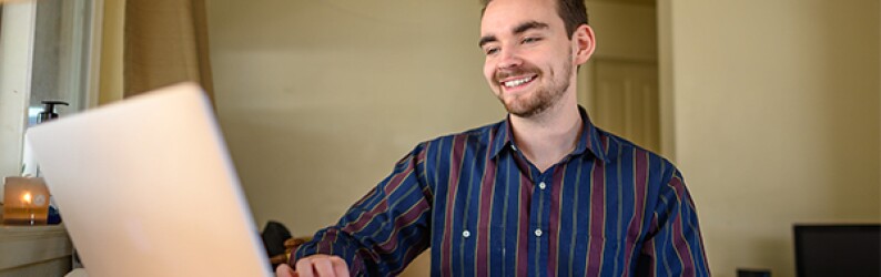 Business student smiling while completing coursework on laptop at home