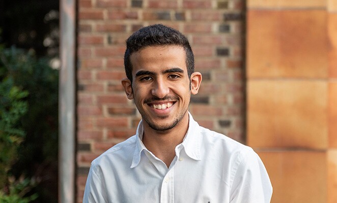 Male Chico State student in white button-down shirt standing in front of brick building on campus