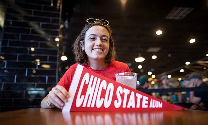 Female Chico State student with red shirt holding sign that says "Chico State Alum"